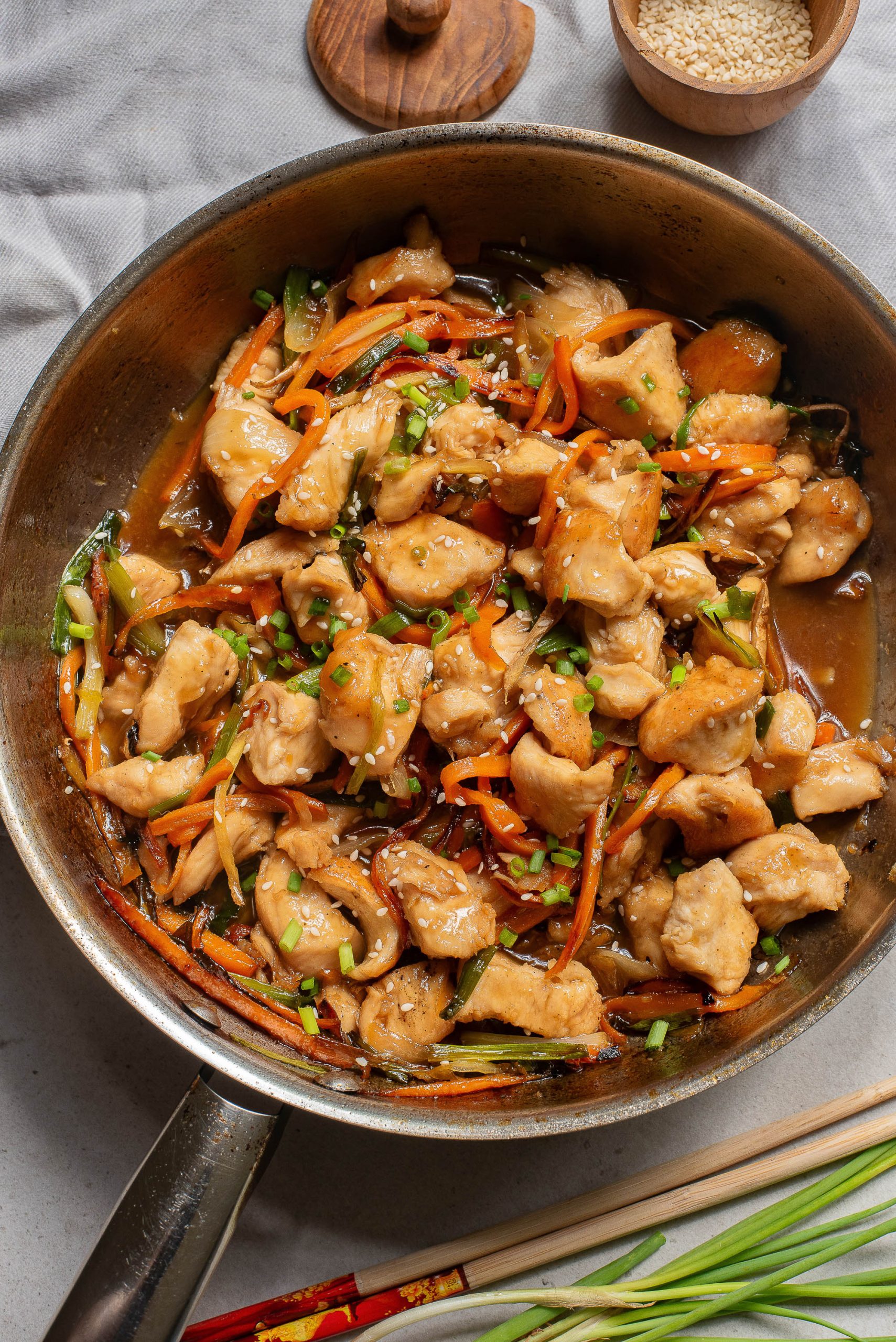 Chinese chicken stir fry in a skillet with carrots and chopsticks.