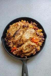 Chicken and rice in a skillet on a grey background.