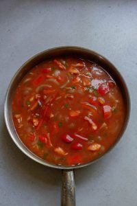 A pan full of soup with vegetables and peppers.