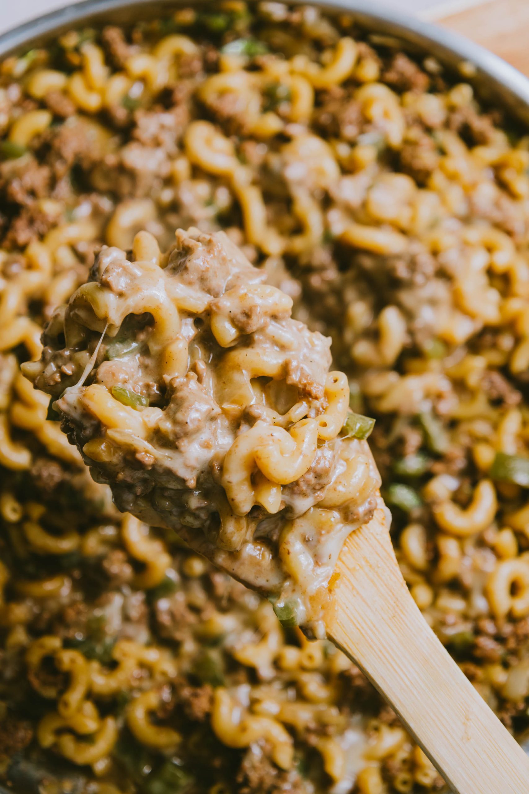 A wooden spoon is being used to scoop Ground Beef Philly Cheesesteak Casserole out of a pan.