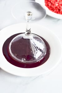 A white plate with a glass of red wine on it.