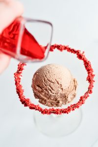 A person is pouring red syrup into a glass of ice cream.