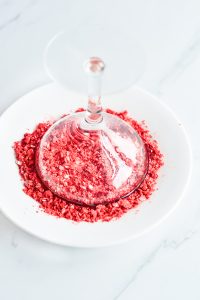 A wine glass filled with red sprinkles on a white plate.