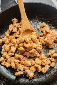 A wooden spoon is being used to stir chicken in a frying pan.