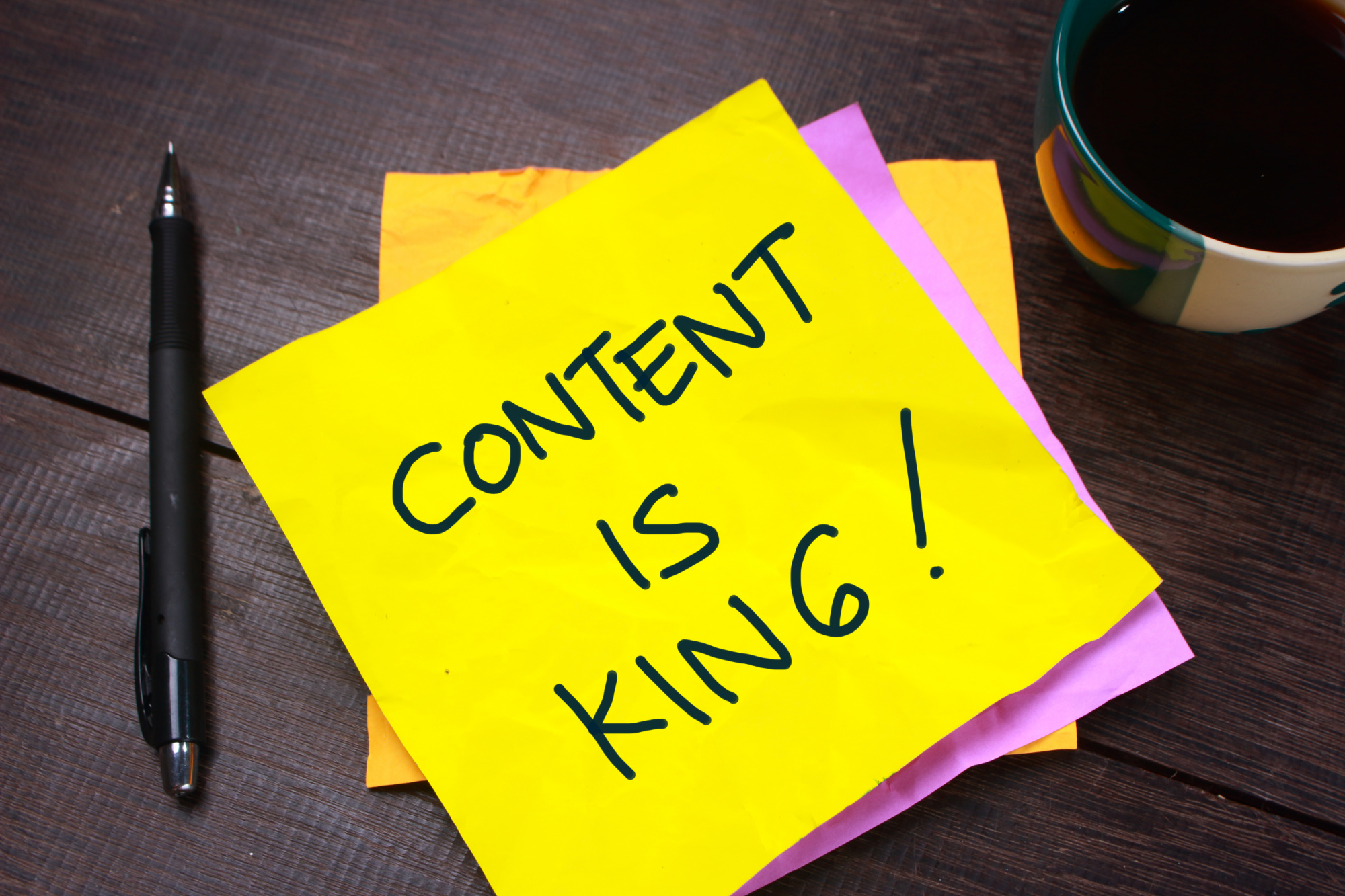 A sticky note with the word content is king next to a cup of coffee.