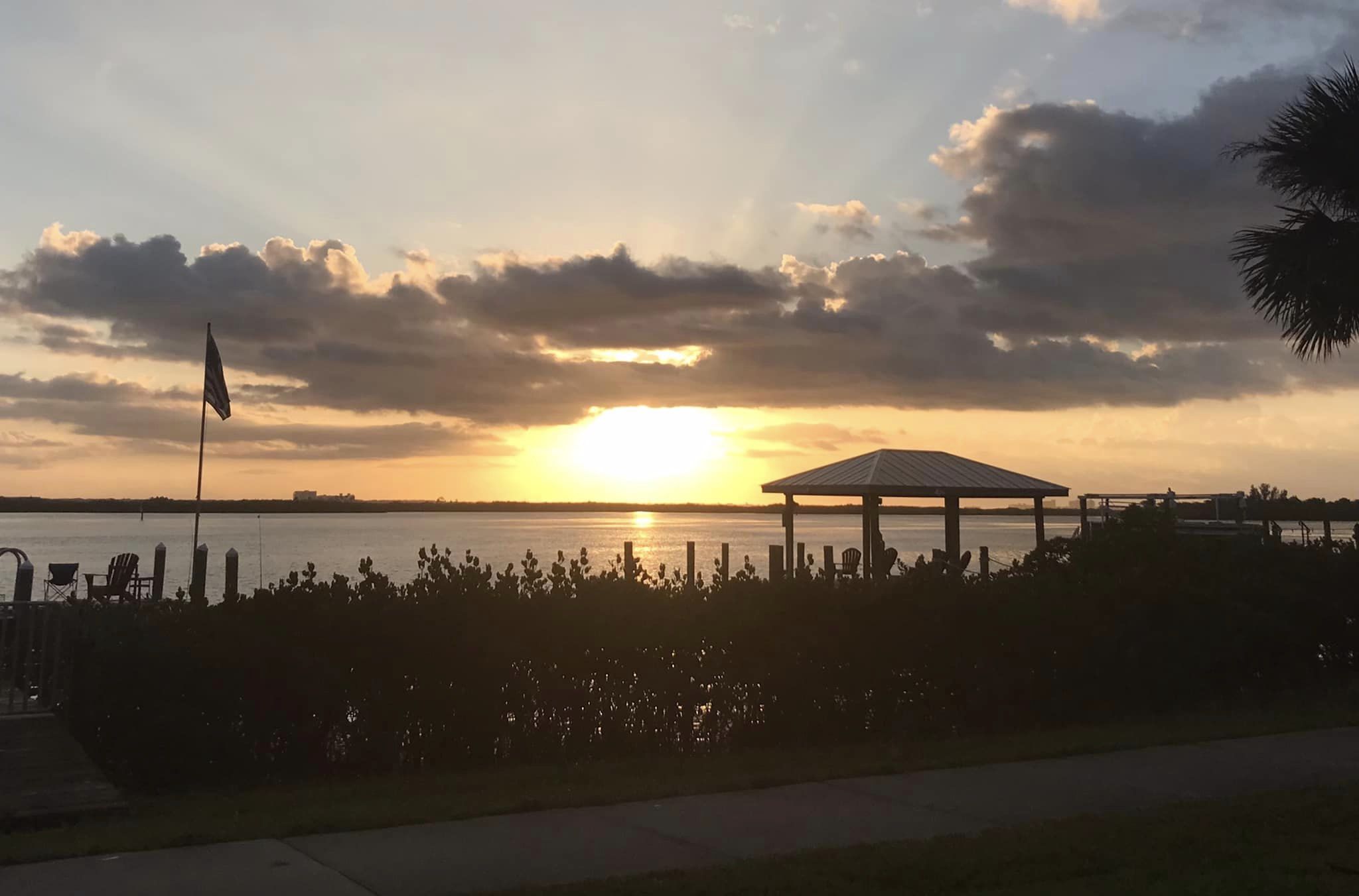 The sun is setting over a body of water with palm trees.