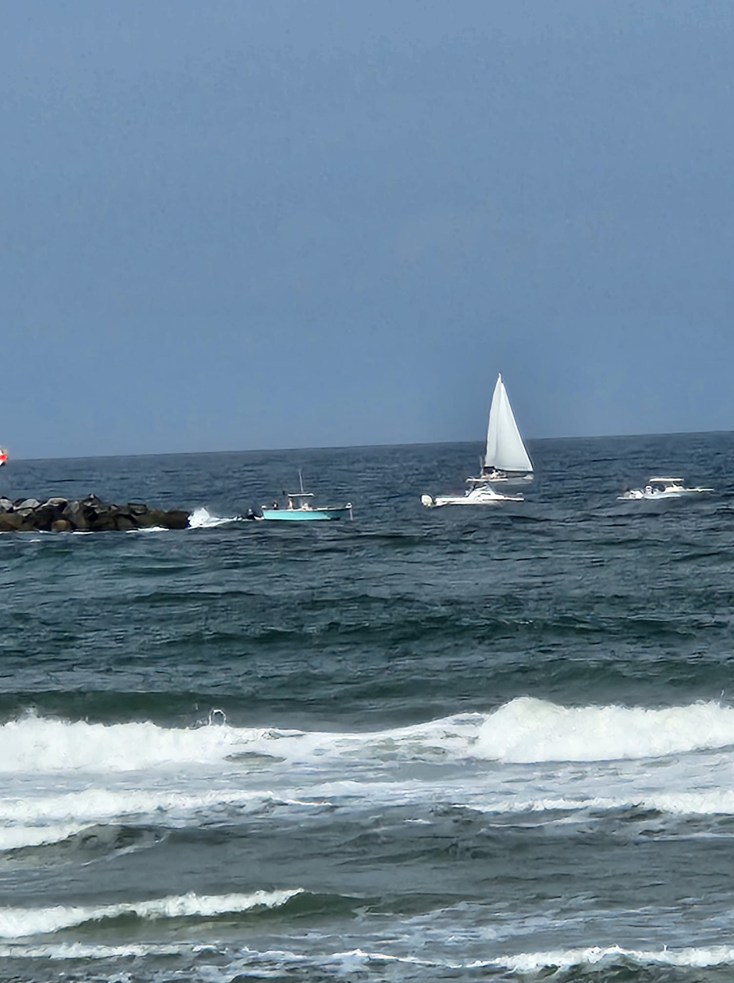 A group of sailboats in the ocean near a rocky shore.