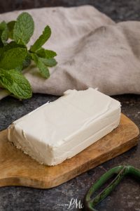 A block of cream cheese substitute on a wooden cutting board with fresh mint leaves and a linen cloth in the background.