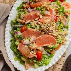 A fresh salad with grapefruit slices, cherry tomatoes, onions, mixed greens, and chopped nuts, served on a decorative plate.