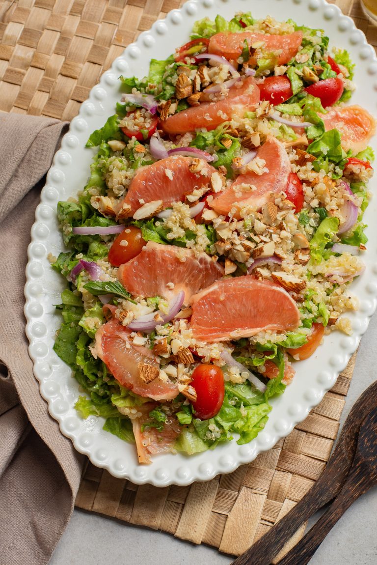 A fresh salad with grapefruit slices, cherry tomatoes, onions, mixed greens, and chopped nuts, served on a decorative plate.