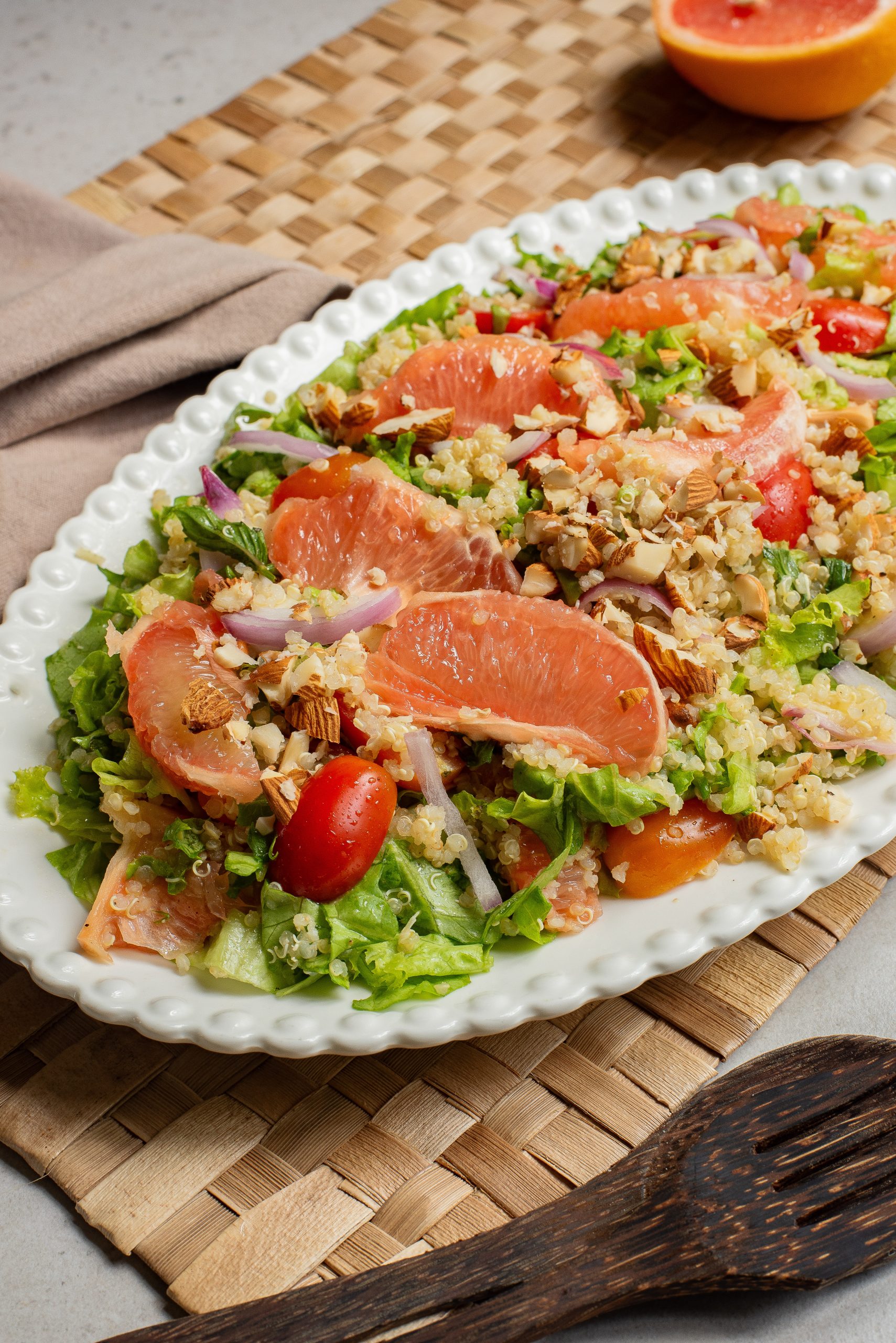 A plate of quinoa salad garnished with grapefruit slices, cherry tomatoes, and nuts on a woven placemat.