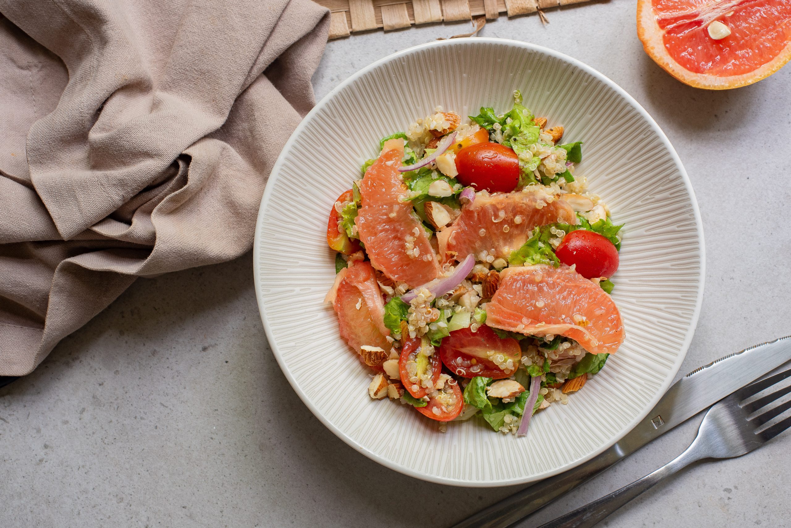 A fresh citrus salad with grapefruit, garnished with cherry tomatoes and sesame seeds, served on a plate.