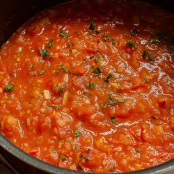 A pot of tomato sauce with herbs on a stove.