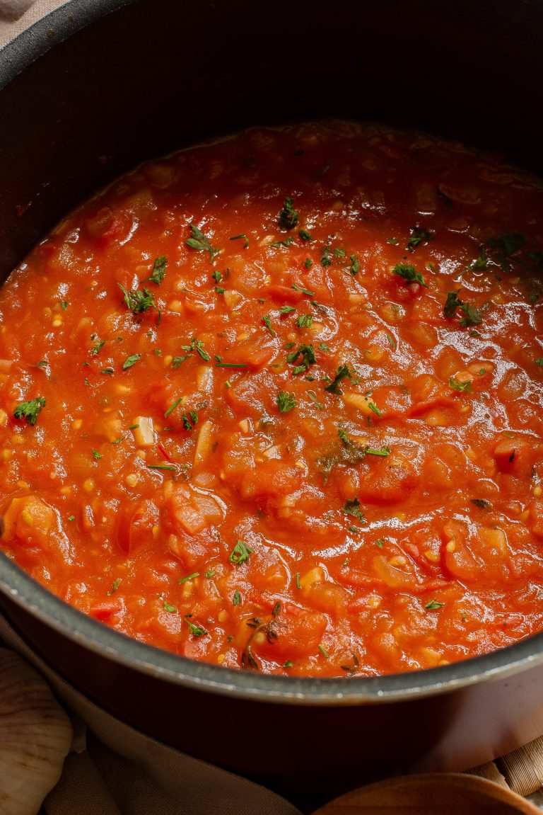 A pot of tomato sauce with herbs on a stove.