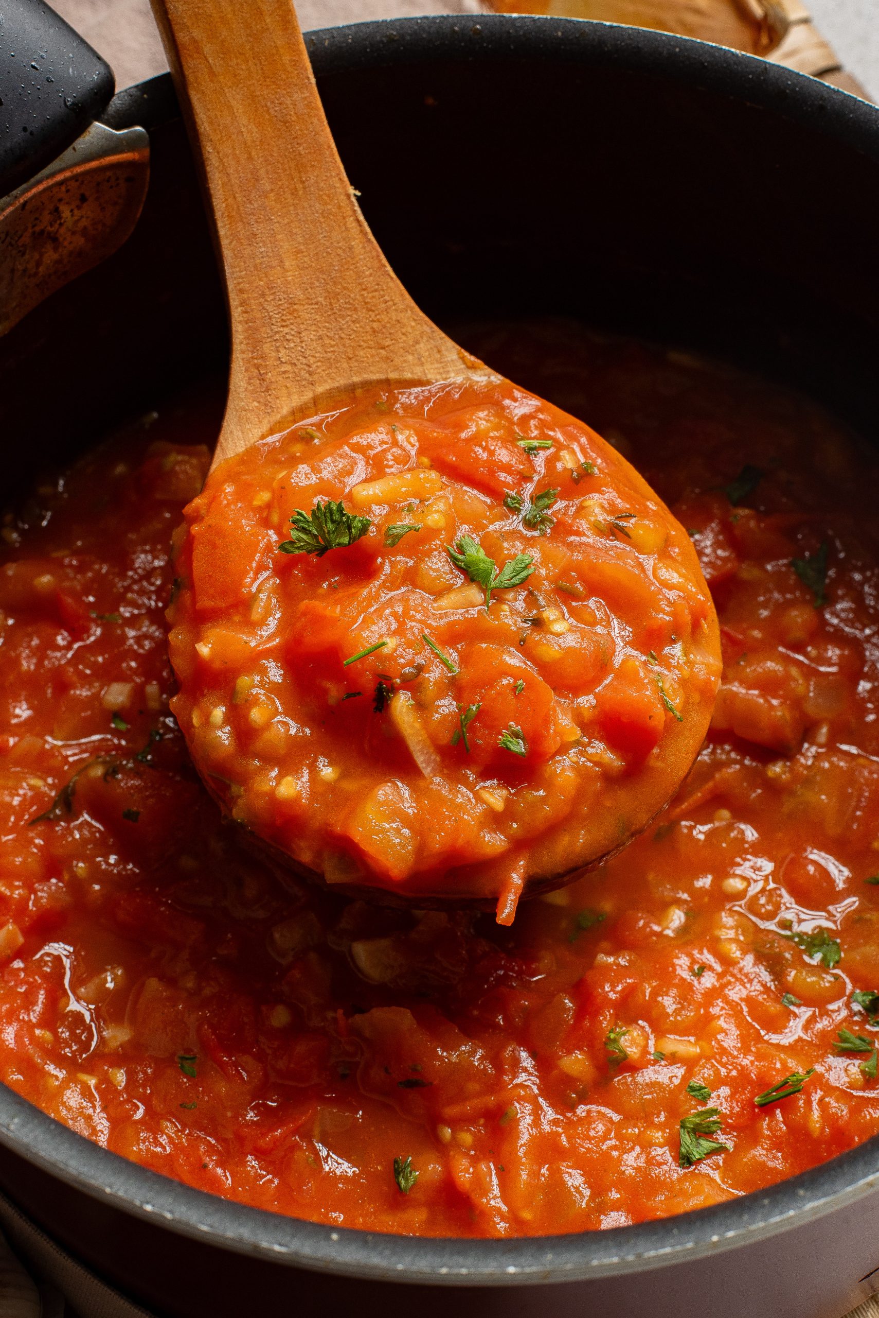 A wooden spoon scooping tomato sauce with vegetables from a pot.
