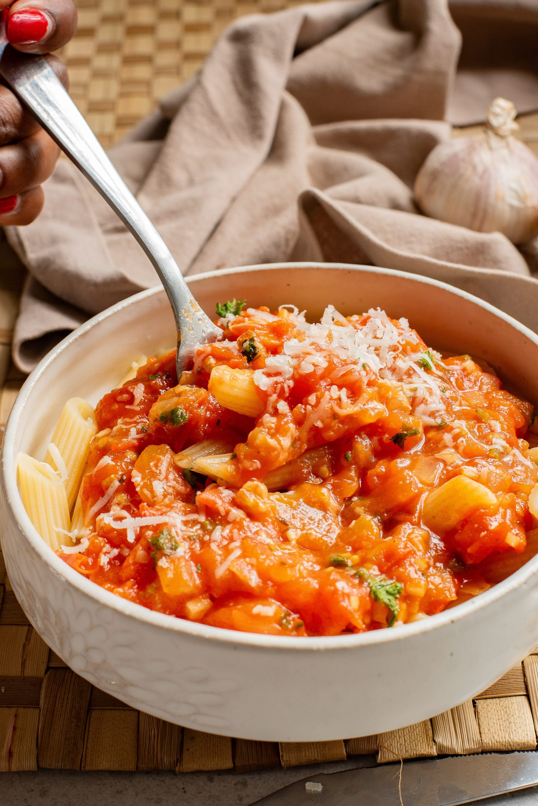 Bowl of penne pasta with tomato sauce and grated cheese, garnished with herbs, with a fork.