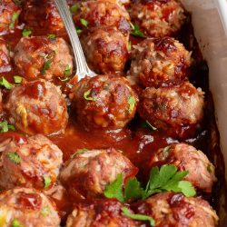 Meatballs in a baking dish with a spoon.