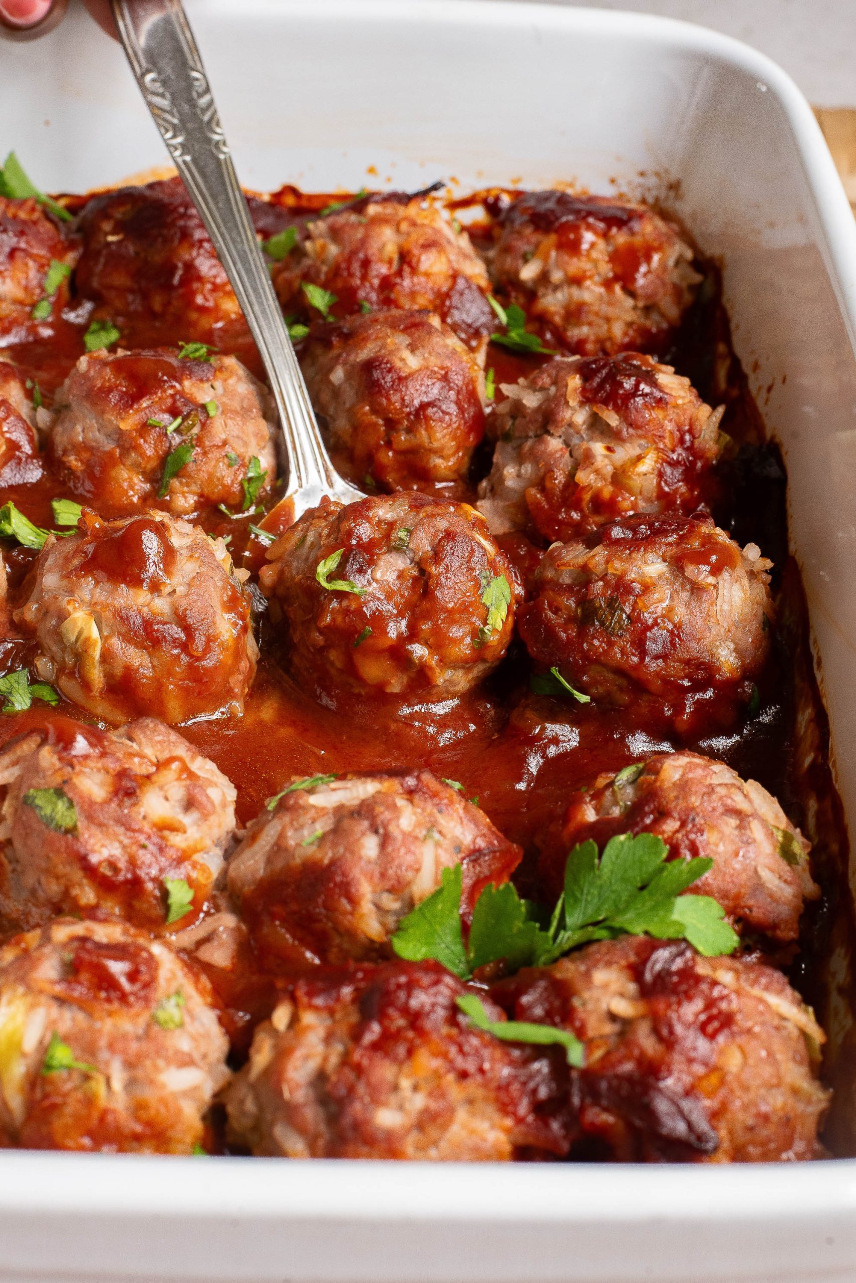 Meatballs in a baking dish with a spoon.
