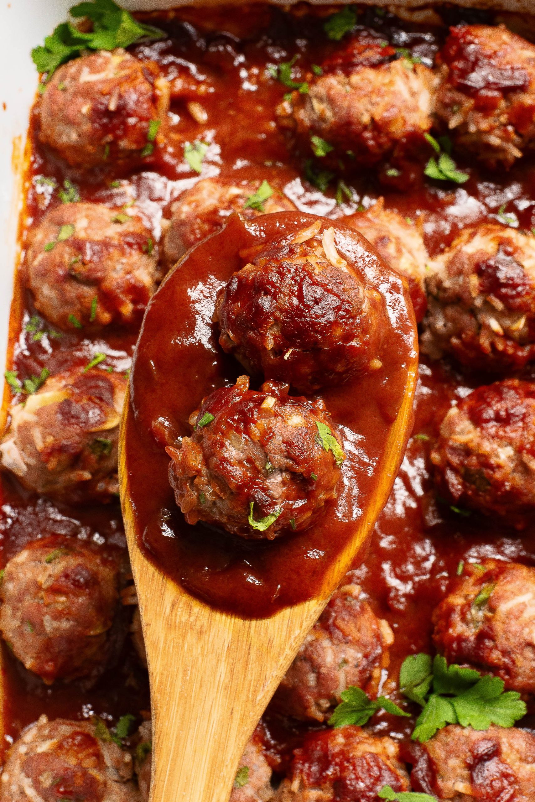 A wooden spoon with bbq meatballs in a casserole dish.
