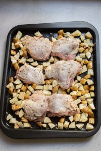 Chicken thighs and diced potatoes arranged on a baking tray ready for cooking.