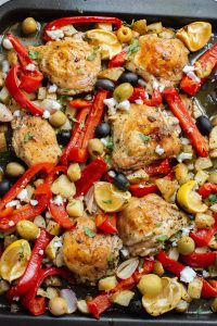 Roasted chicken thighs with bell peppers, olives, and herbs in a baking dish.