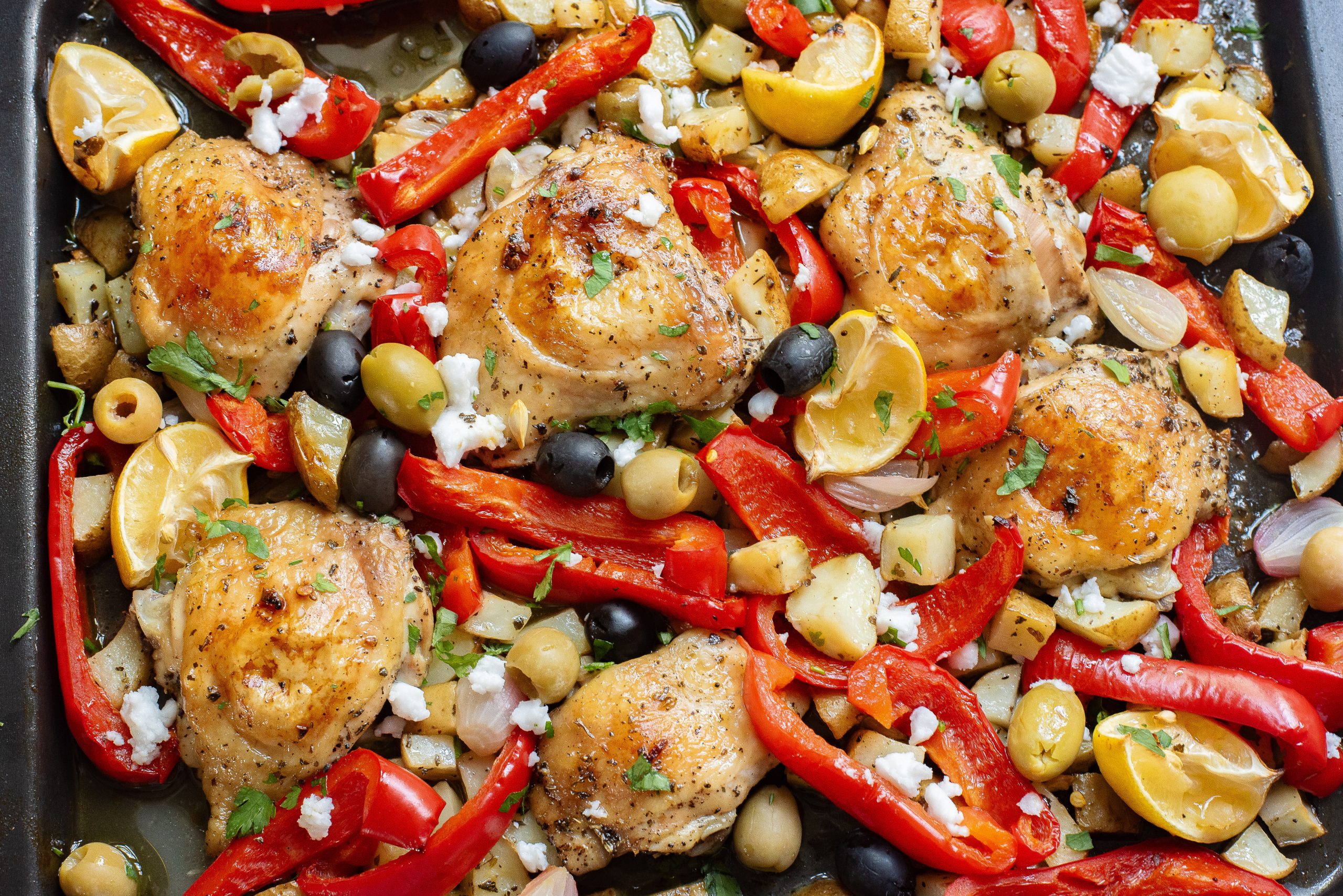 Sheet Pan Greek Chicken Thighs  with bell peppers, olives, garlic, and feta cheese on a baking sheet.