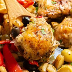 Roasted chicken pieces with mixed bell peppers, olives, and herbs in a baking dish.
