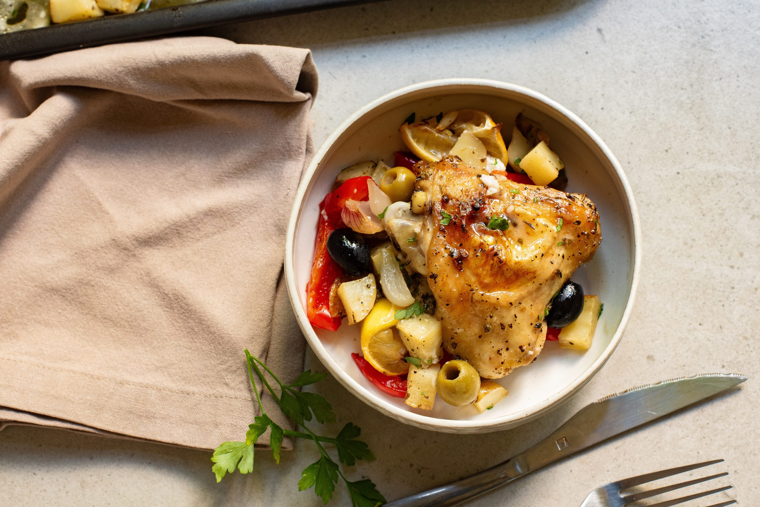 Grilled chicken breast served with a side of pasta, tomatoes, olives, and garnished with parsley.