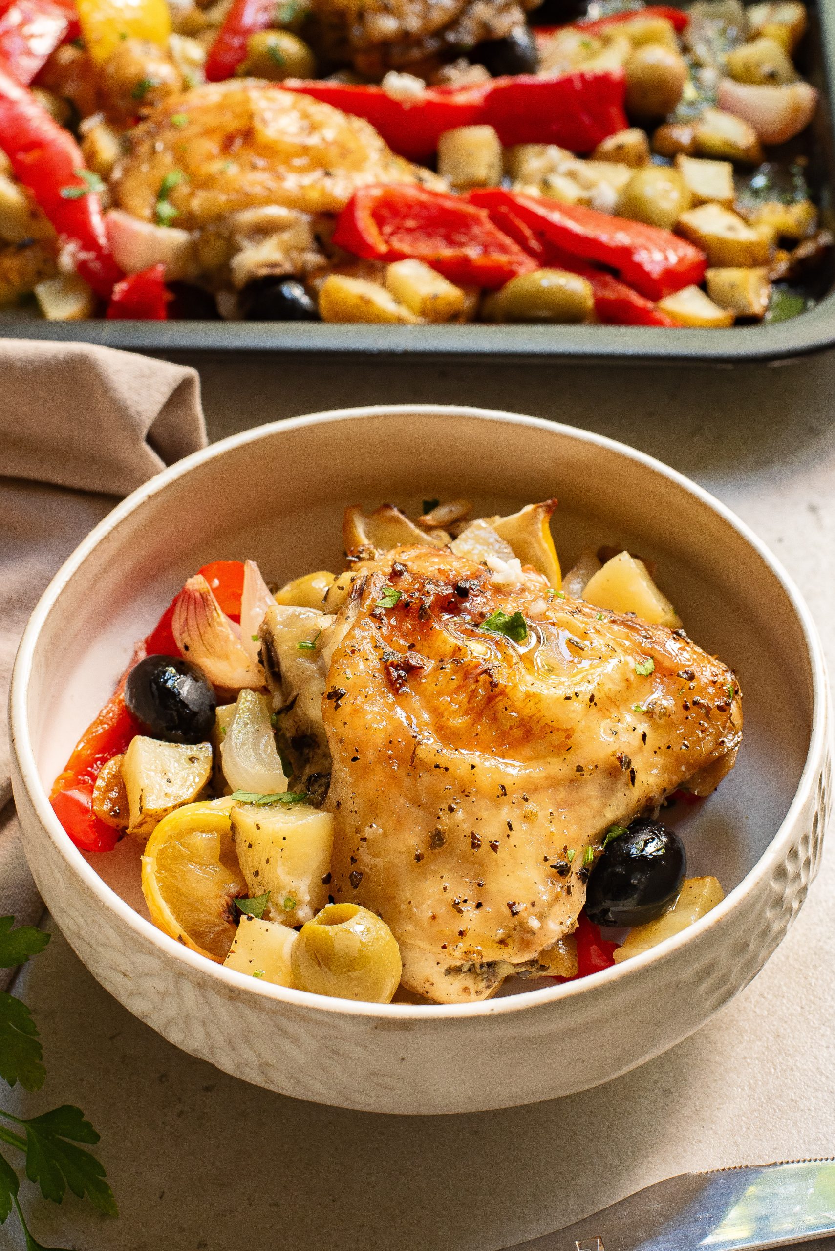 Sheet Pan Greek Chicken Thighs h served with roasted vegetables and olives in a bowl.