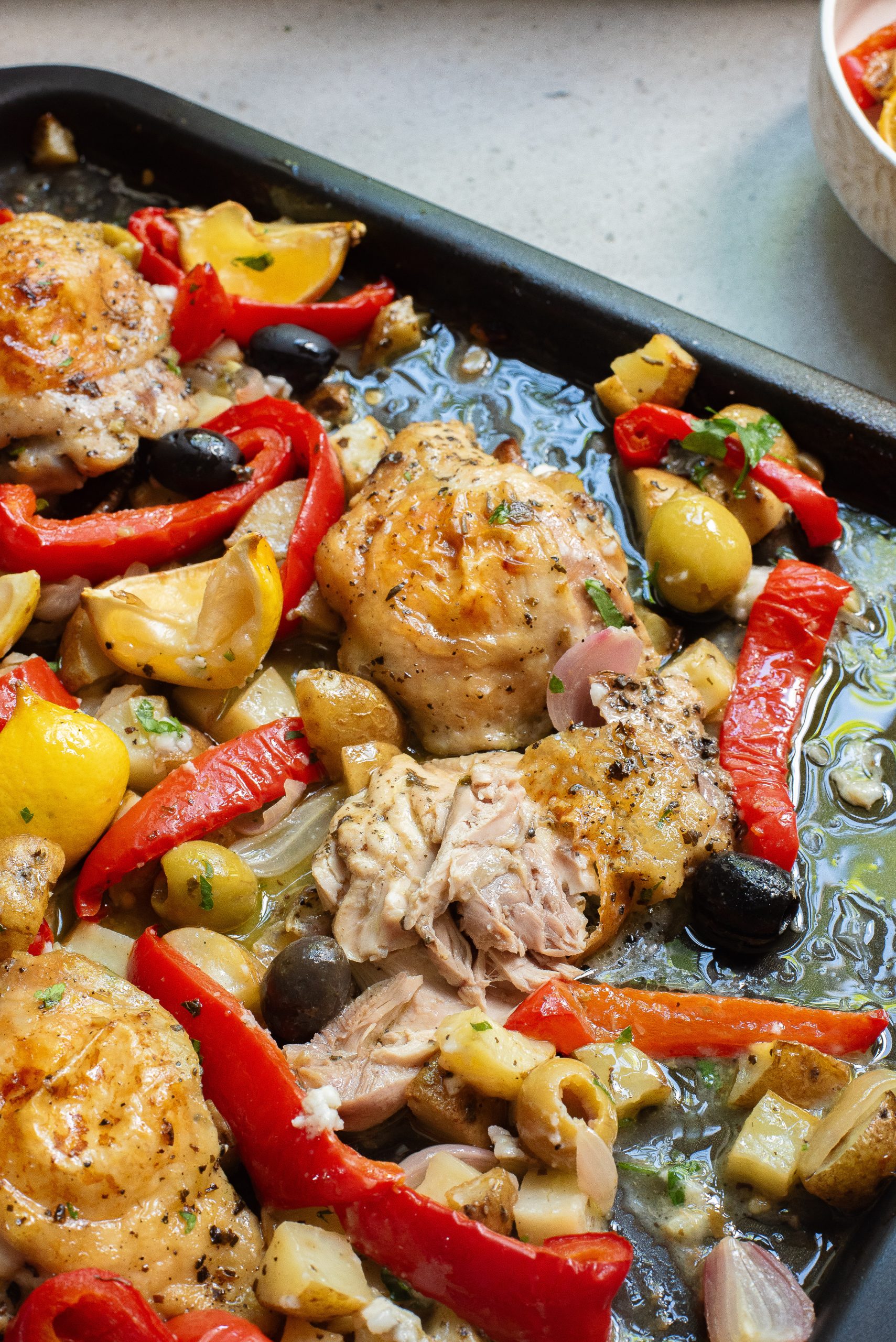 Roasted chicken thighs and mediterranean vegetables on a baking sheet.