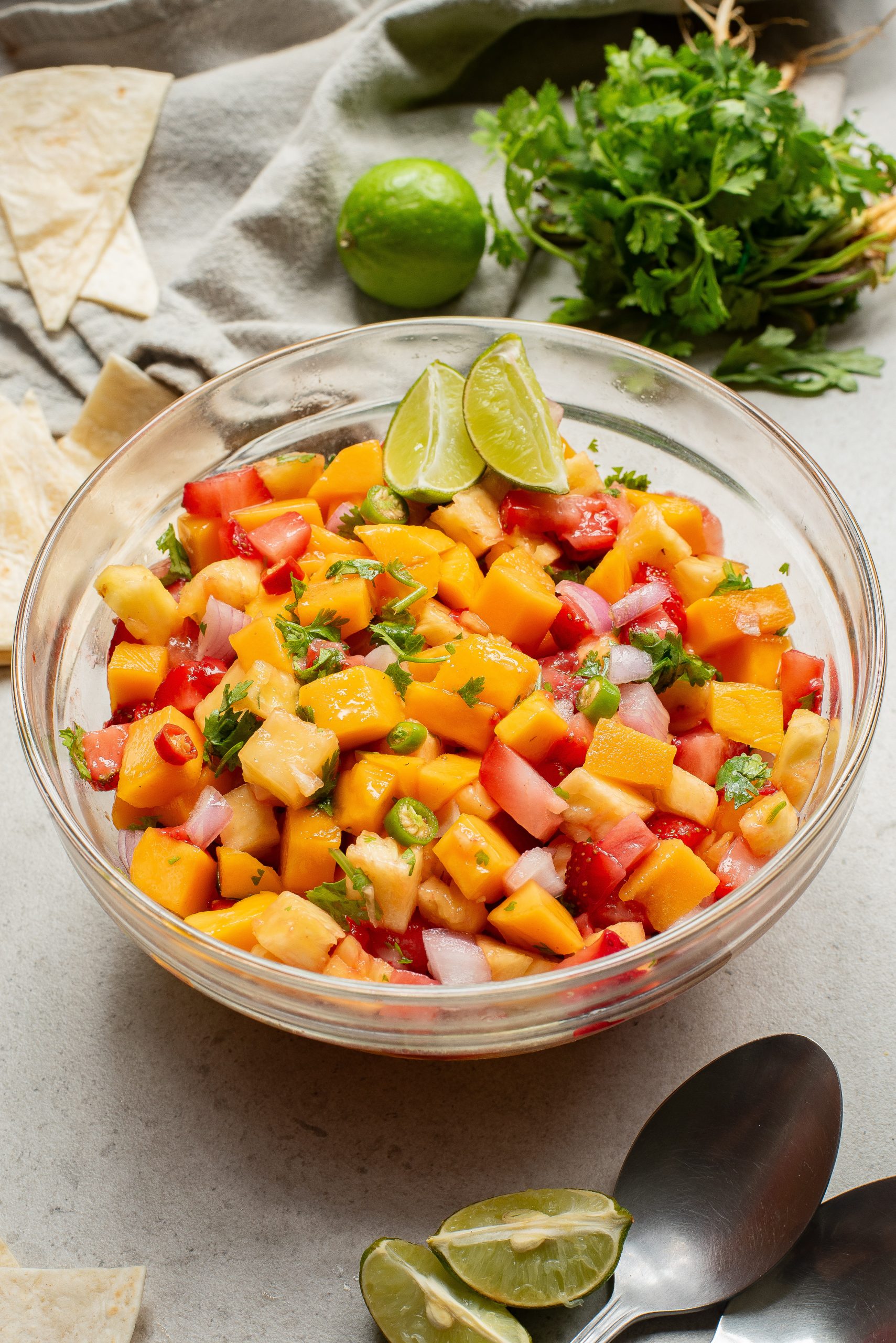 A bowl of fresh mango salsa with lime wedges and tortilla chips on a kitchen countertop.