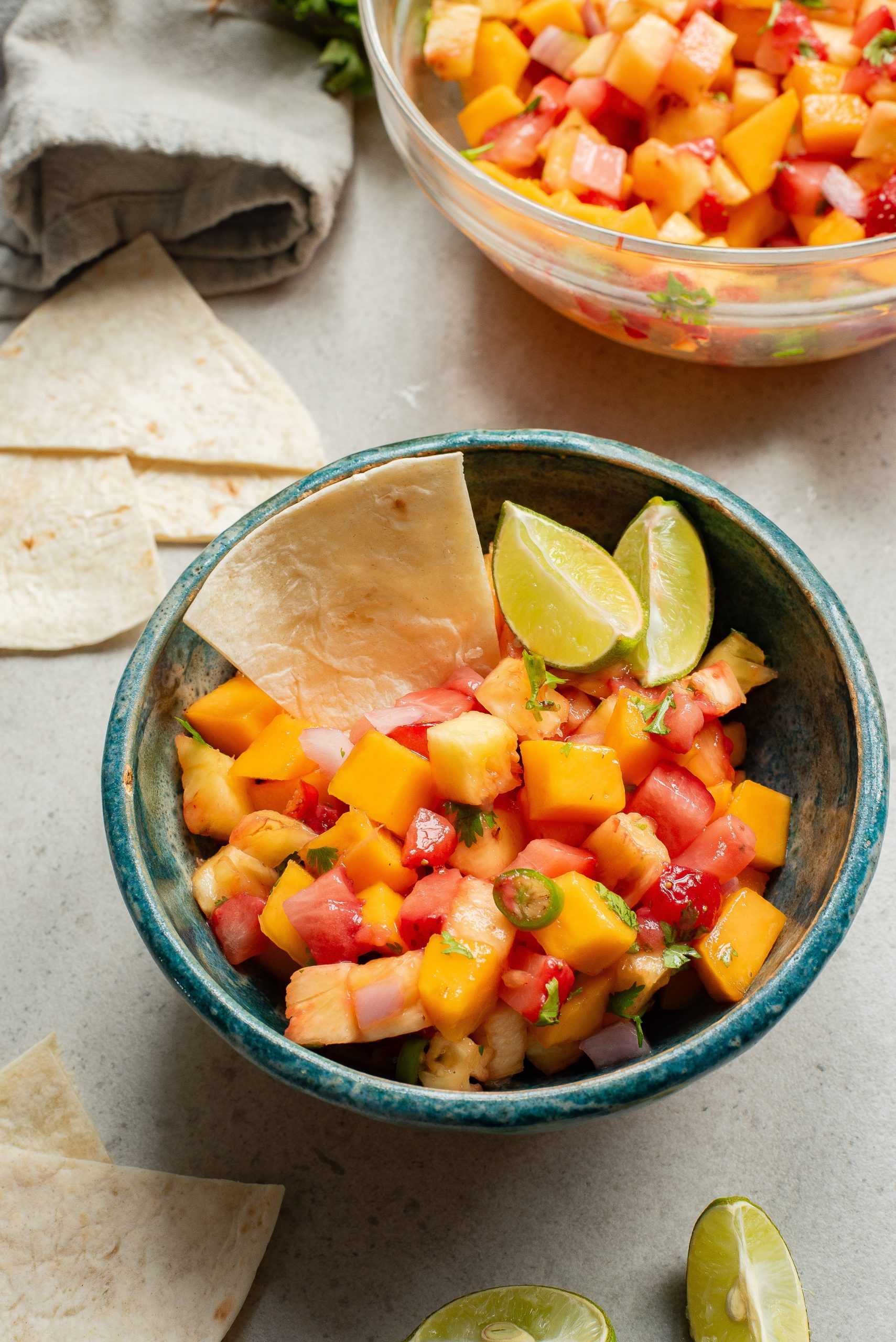 A bowl of fresh mango salsa with lime wedges and tortilla chips on a table.