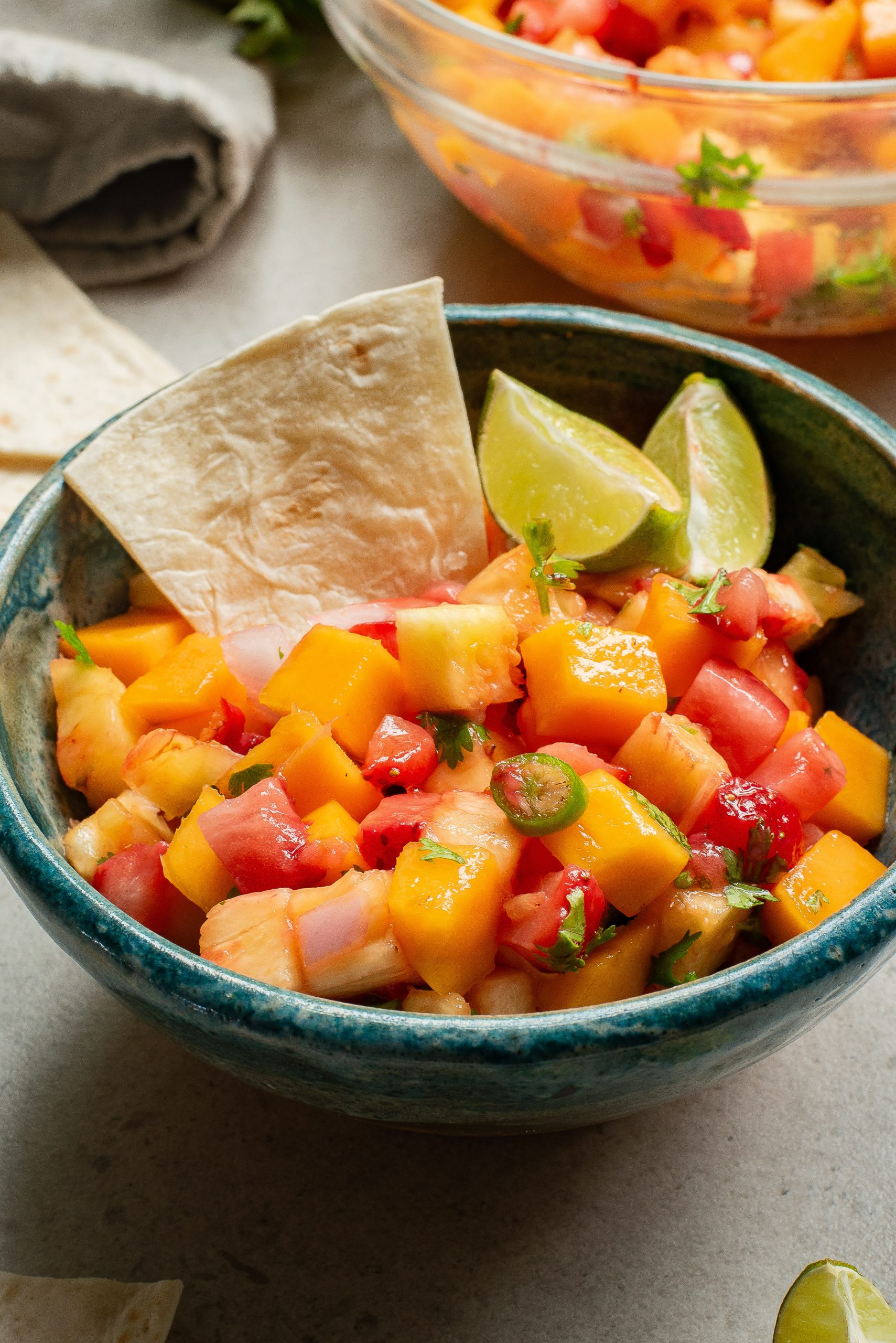 A bowl of salad with lime wedges and a tortilla chip.