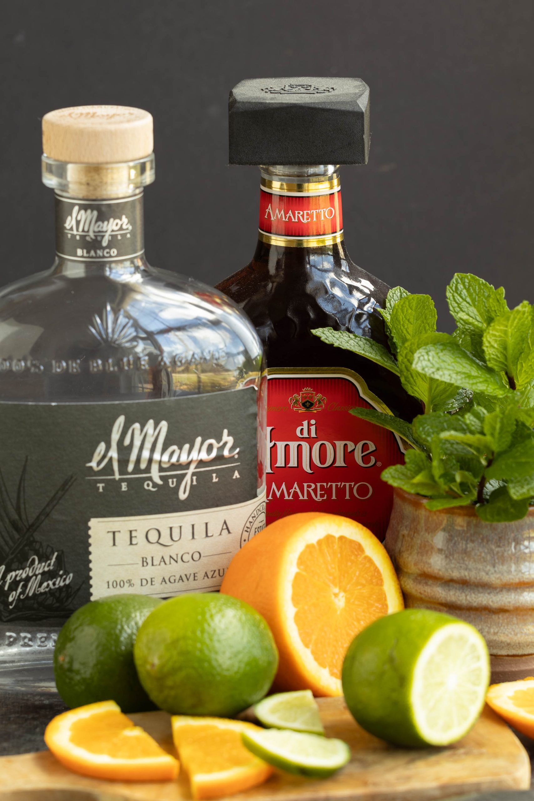 Bottles of el mayor blanco tequila and amaretto di amore with fresh citrus and mint leaves.
