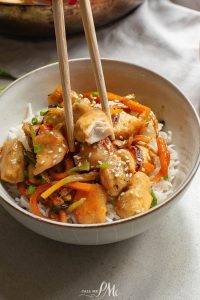 A bowl of stir-fried chicken and vegetables over rice, garnished with sesame seeds.
