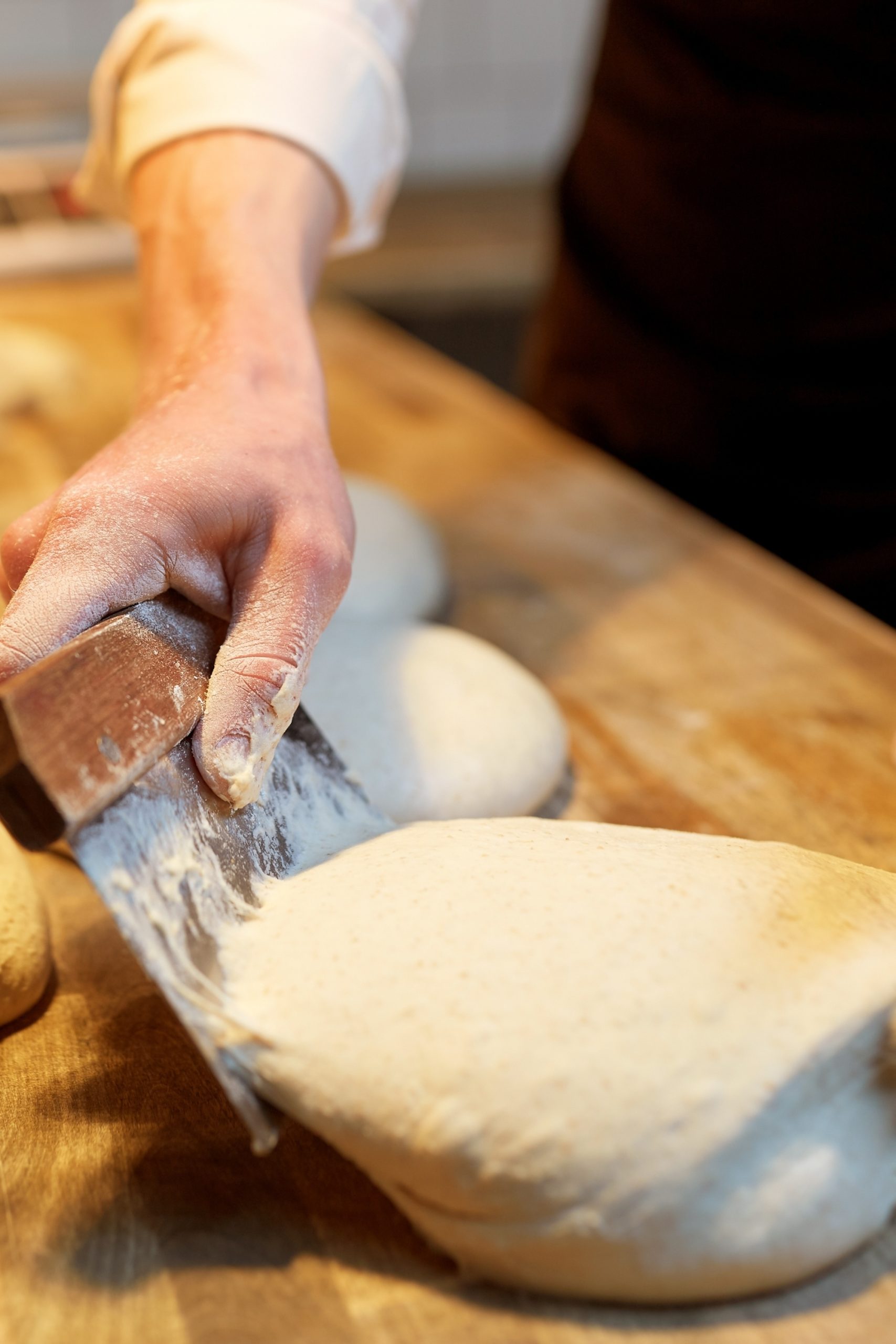 A person dividing freezing yeast bread dough with a bench scraper on a floured surface.