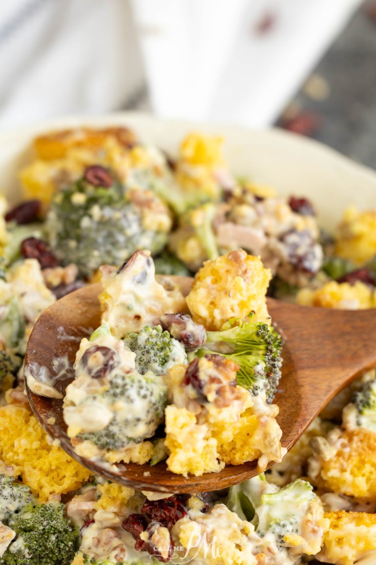 A wooden spoon scooping broccoli and cauliflower salad with cranberries and creamy dressing from a serving bowl.