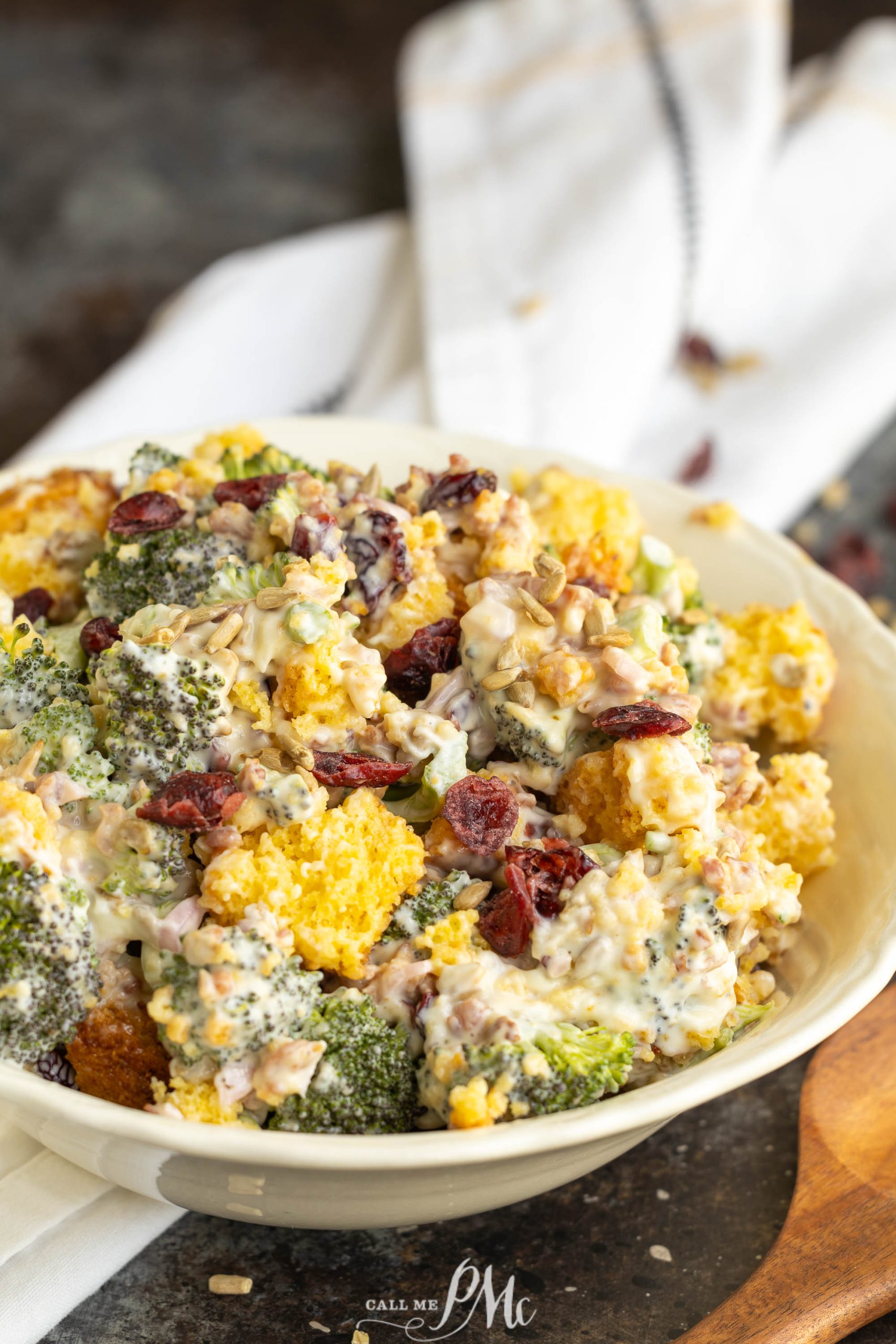 A bowl of broccoli and cauliflower salad with dried cranberries and a creamy dressing, served on a rustic table.