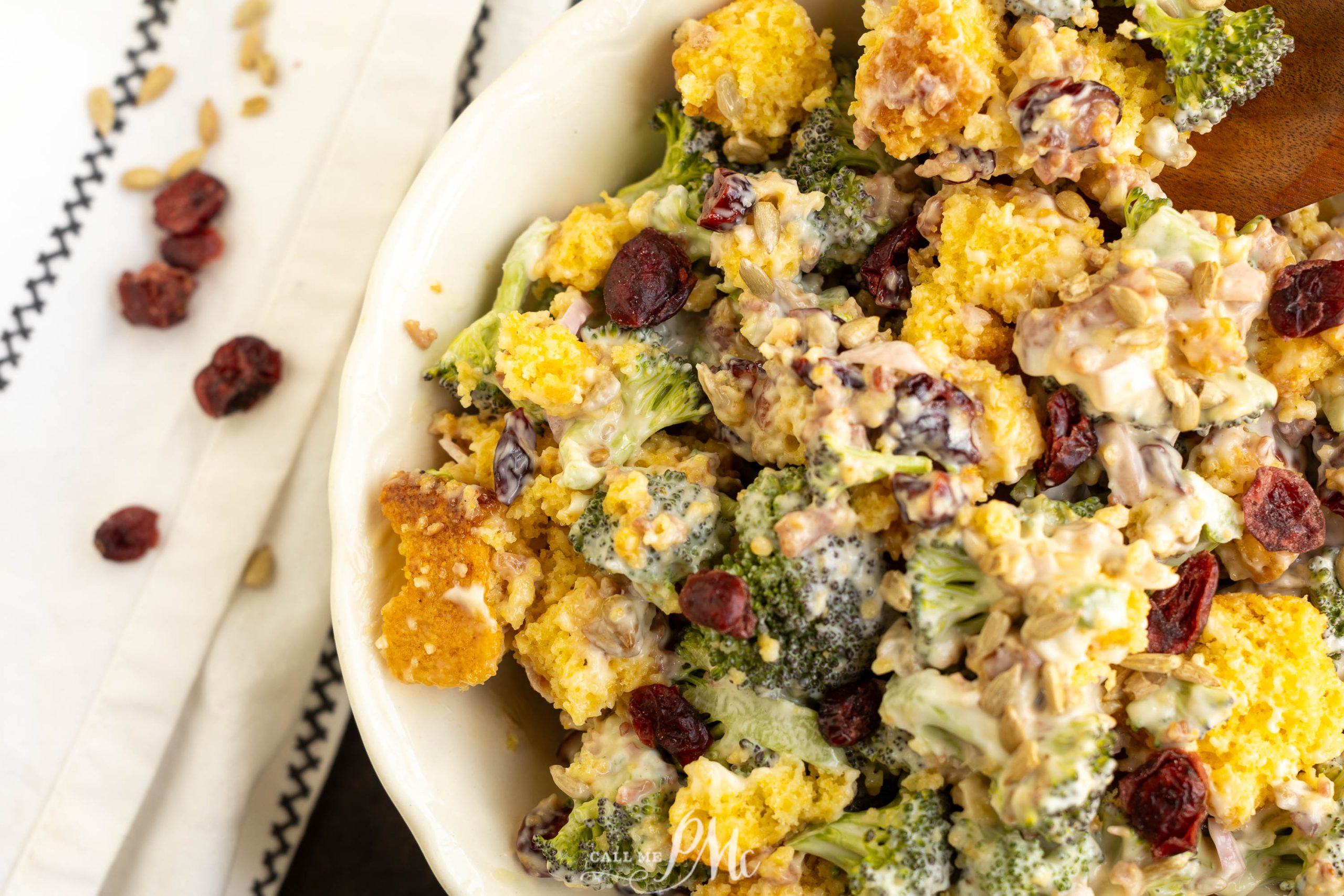 Close-up view of a side dish with dried cranberries, sunflower seeds, and a creamy dressing in a white bowl.