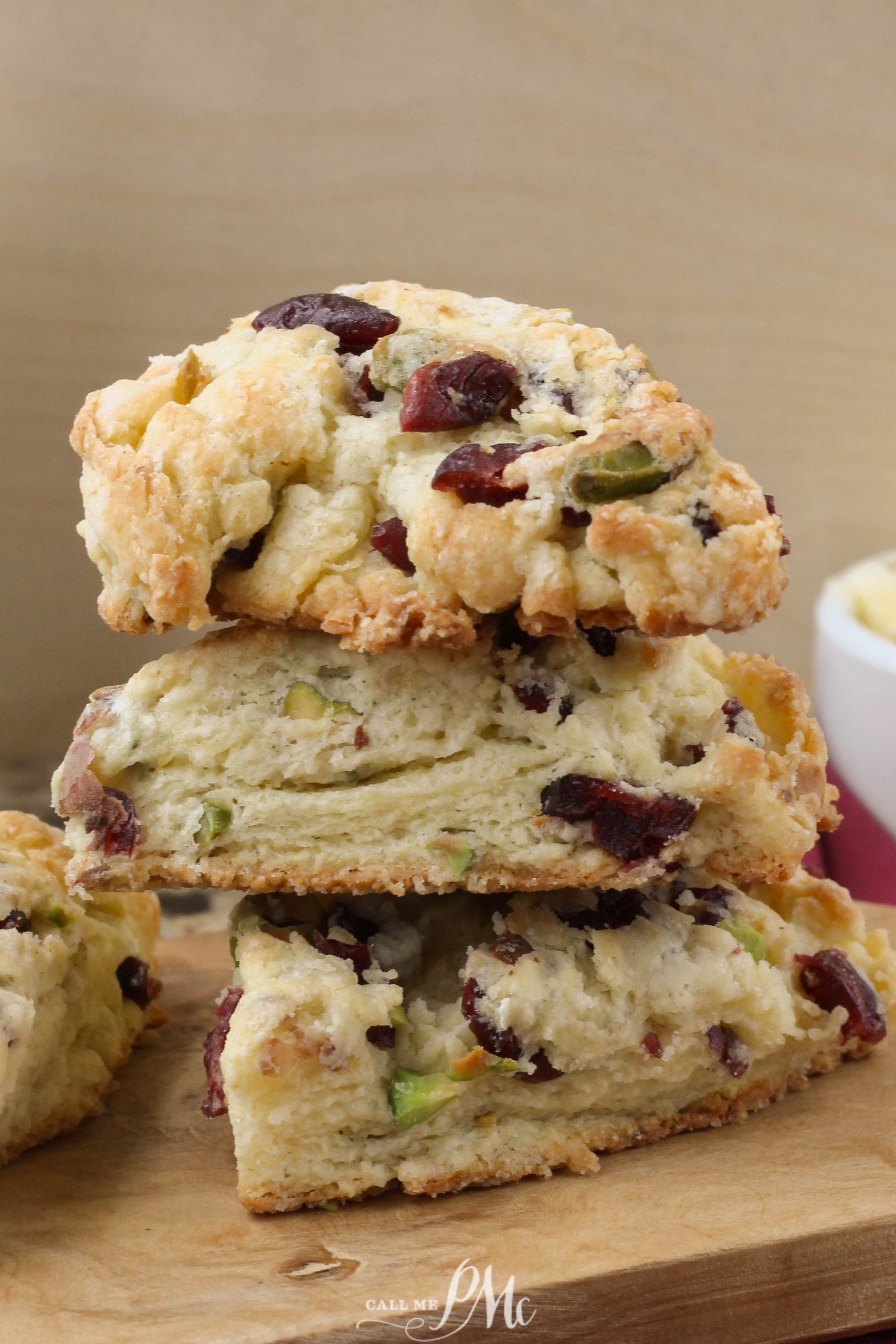 A stack of three Dried Cherry Pistachio Scones on a wooden table, with visible pieces of cranberries and pistachios.