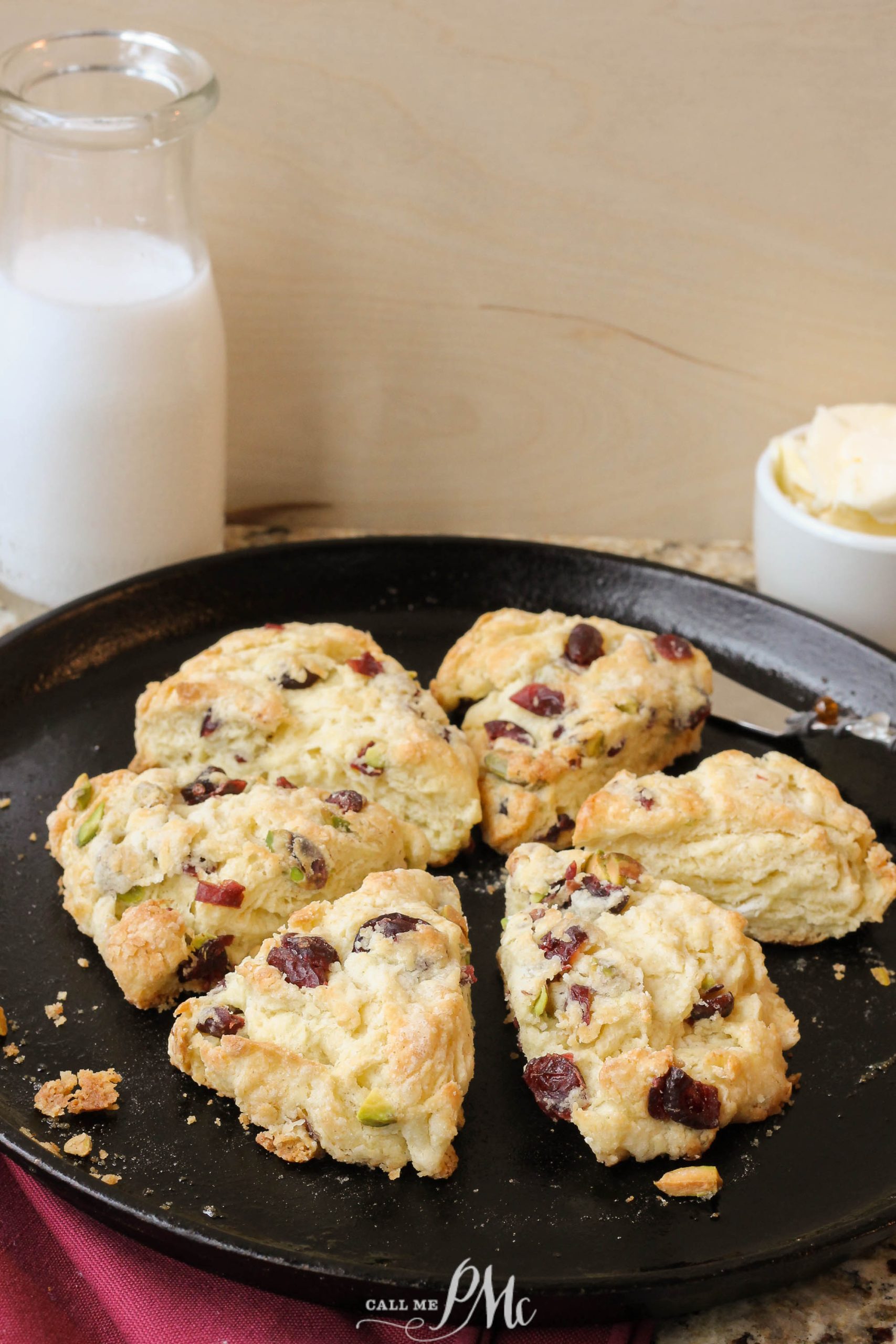 Freshly baked scones with cranberries and nuts on a black plate, with a glass milk bottle and butter in the background.