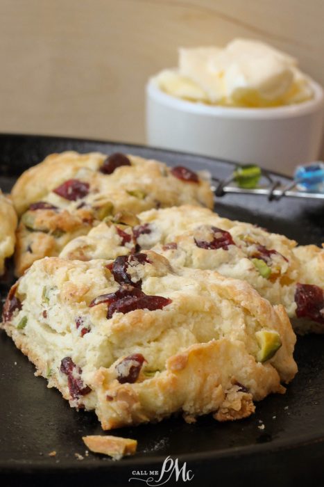 Freshly baked scone with cranberries and pistachios on a skillet, served with a side of butter.