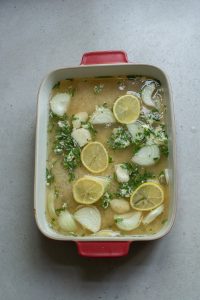 Baking dish with onion soup garnished with lemon slices and chopped parsley on a gray surface.