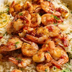 Grilled shrimp on a bed of lemon rice garnished with herbs in a red baking dish.