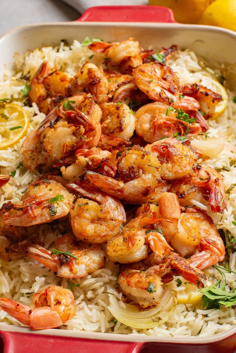 Grilled shrimp on a bed of lemon rice garnished with herbs in a red baking dish.
