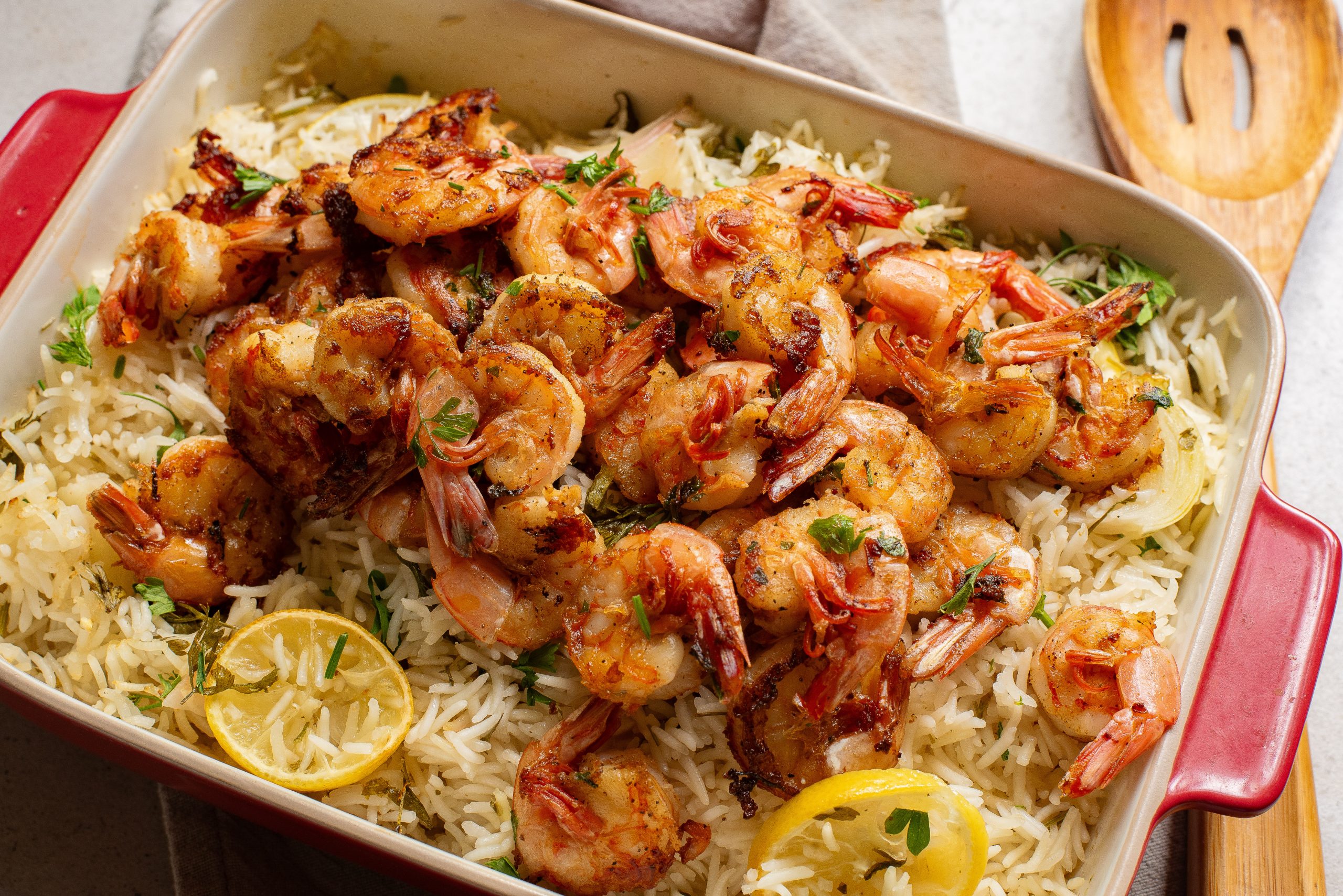 Grilled shrimp on a bed of lemon rice garnished with herbs in a red baking dish.