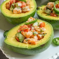 Fresh shrimp ceviche served in halved avocados on a white plate, garnished with cilantro and lime slices.