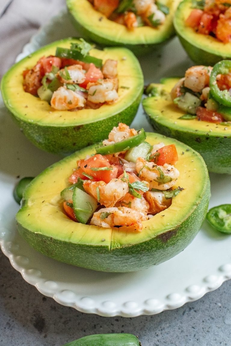 Fresh shrimp ceviche served in halved avocados on a white plate, garnished with cilantro and lime slices.