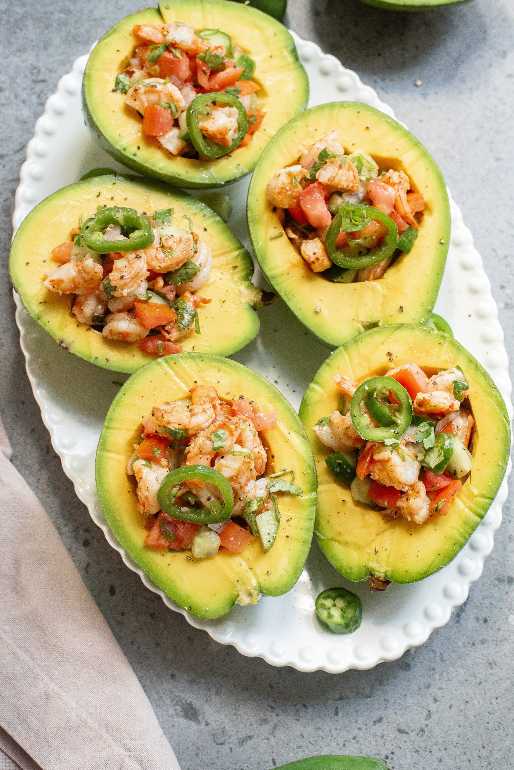 Fresh shrimp ceviche served in halved avocados on a white plate, garnished with cilantro and lime slices.