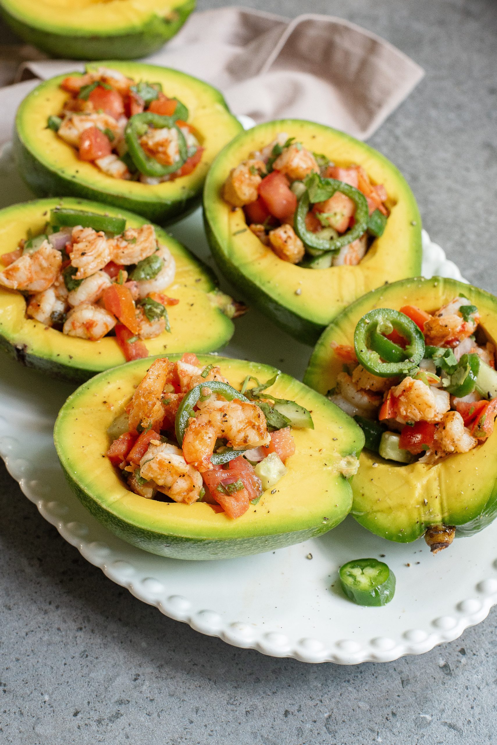 A plate of avocado halves filled with a shrimp and tomato salad, garnished with sliced jalapeños.
